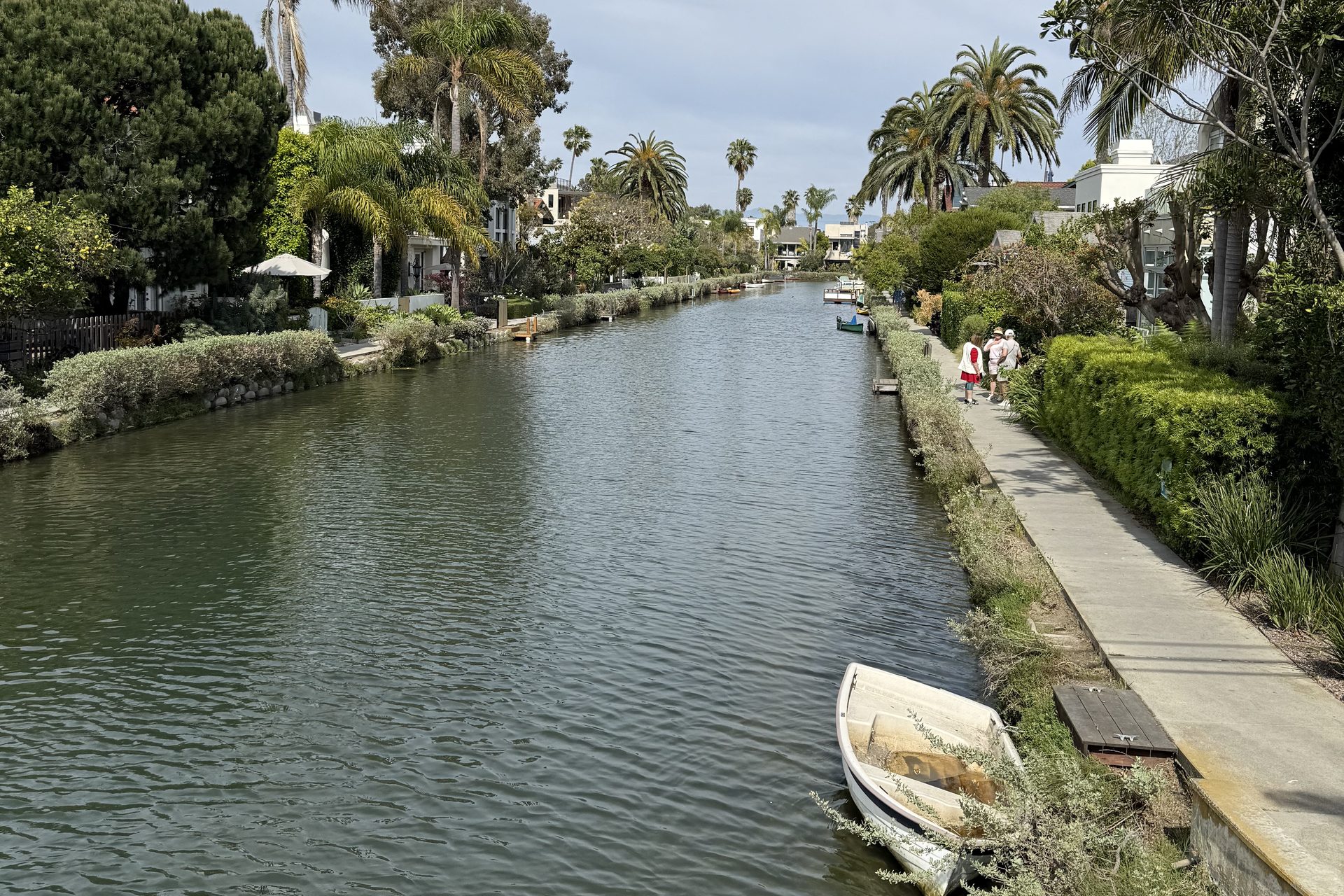 A rowboat moored on a Venice canal, with a footpath and gardens along the bank
