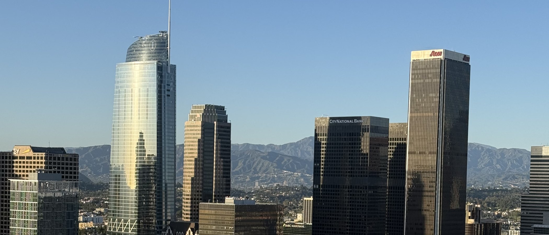 Downtown Los Angeles office towers seen from above, with the San Gabriel Mountains behind