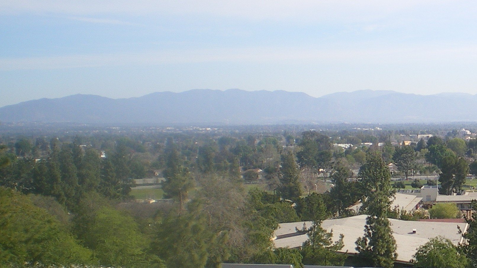 The San Fernando Valley from the roof of Pierce College in Woodland Hills, with tree-covered neighborhoods and campus buildings below hazy mountains