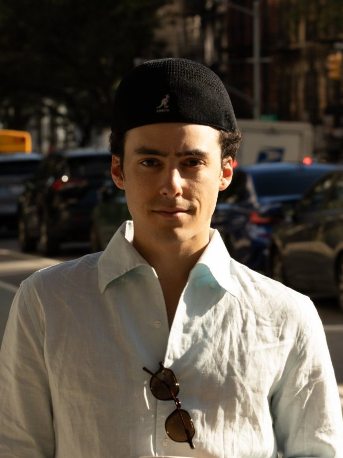 Miles Morton on a street corner in a linen shirt and a black cap