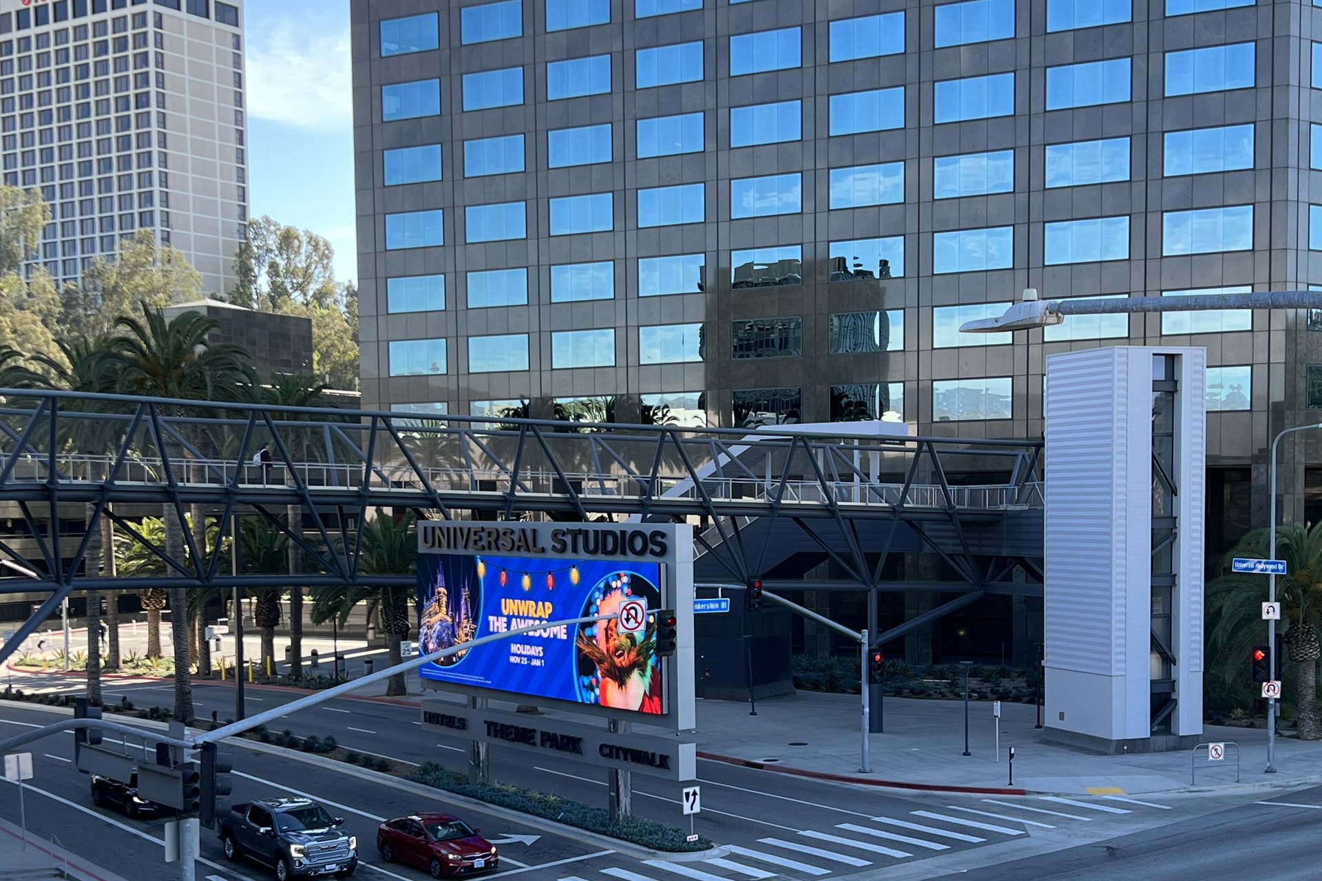 The Universal Studios entrance sign on Universal Hollywood Drive, advertising the theme park, with the Universal City office tower behind it