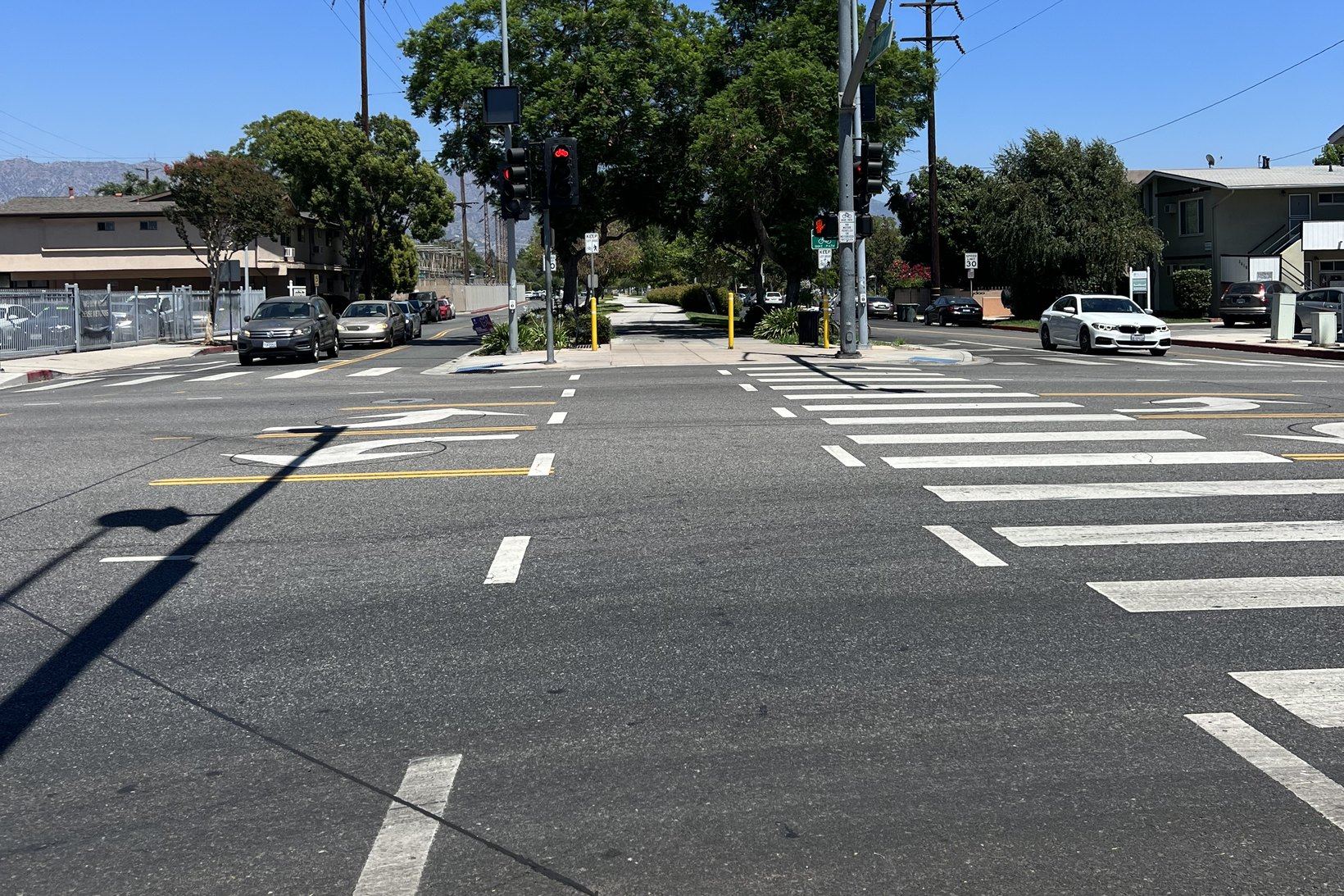 A wide signalized intersection with marked crosswalks, red pedestrian signals and a 30 mile per hour speed limit sign, with the San Gabriel Mountains in the distance